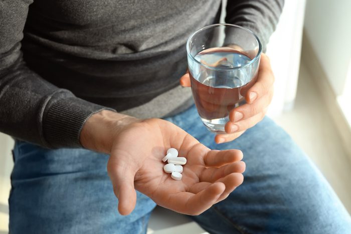 Young man with pills and glass of water at home, closeup