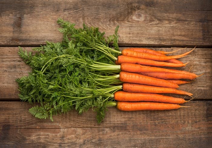 Bunch of fresh carrots with green leaves over wooden background. Vegetable. Food