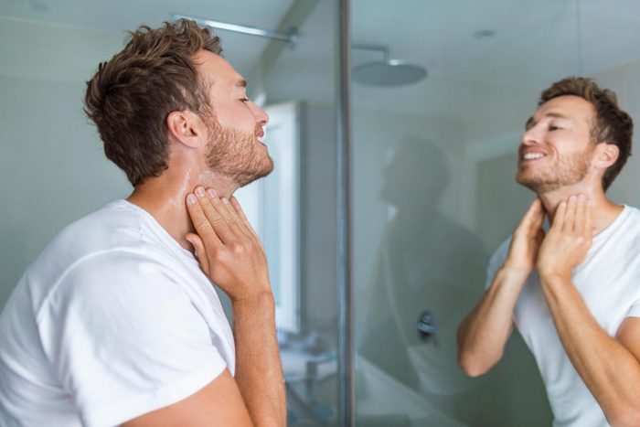 man exfoliating face while looking in mirror