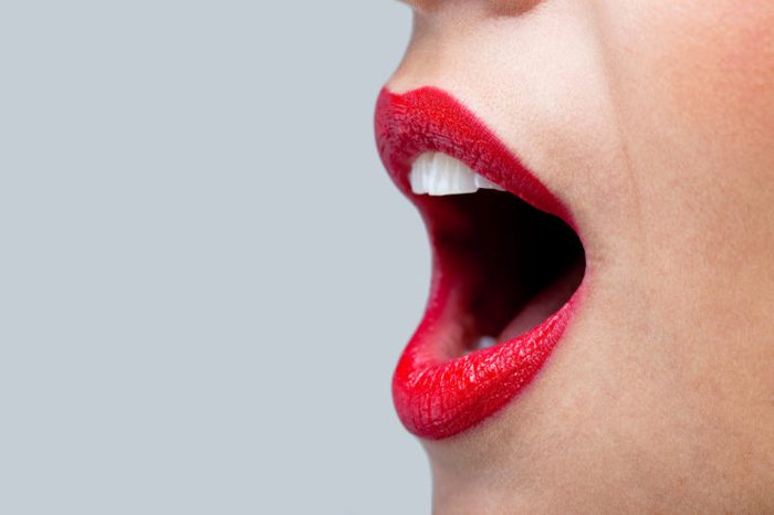 Close up of a womans mouth wide open with bright red lipstick on her lips.