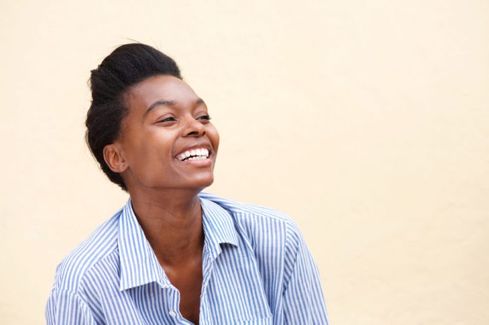 Close up portrait of beautiful young black woman laughing against wall