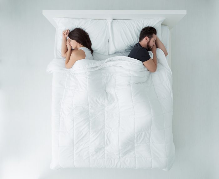 Young couple sleeping in bed back to back, top view