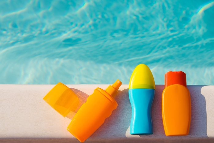 Bottles of sunscreen cream and lotion near swimming pool