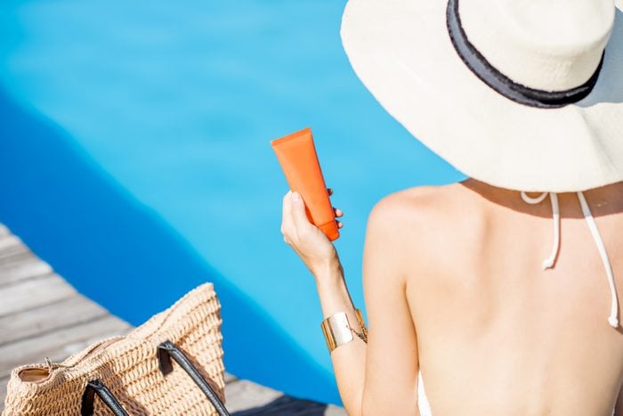 Woman in sun hat sitting with sunscreen near blue water