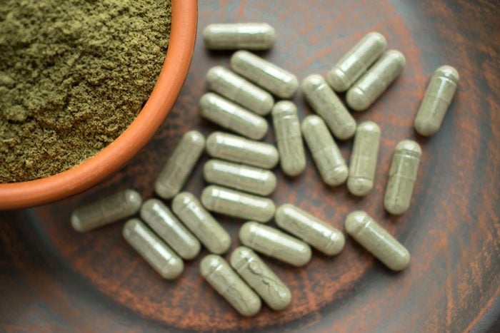 Supplement kratom green capsules and powder on brown plate. Herbal product alt-medicine kratom is opioid. Home alternative pain remedy, opioid addiction, dangerous painkiller. Selective focus