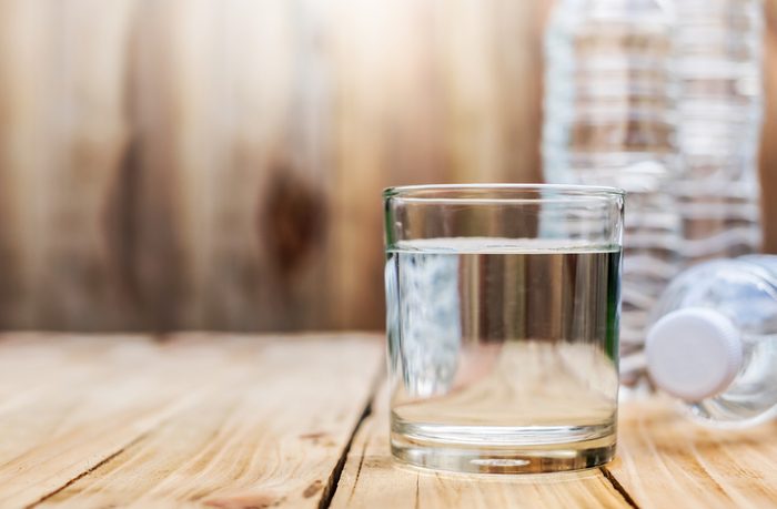 Clear water in a glass and a water bottle rests on a wooden floor. Has a brown wood background.