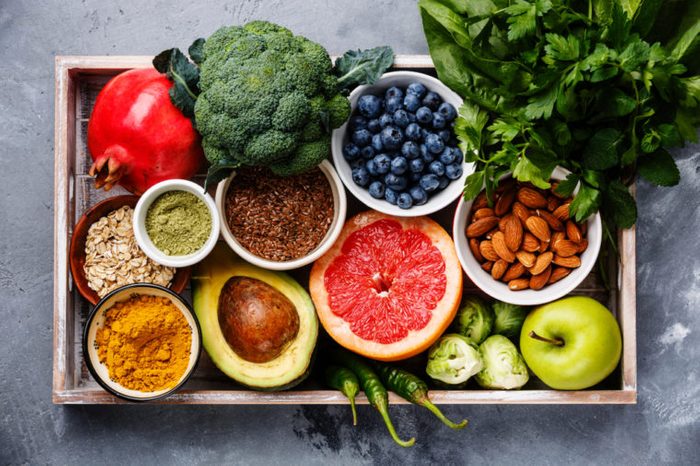 Выбор здоровой пищи в деревянной коробке: фрукты, овощи, семена, суперпродукты, злаки, листовые овощи на сером бетонном фоне
