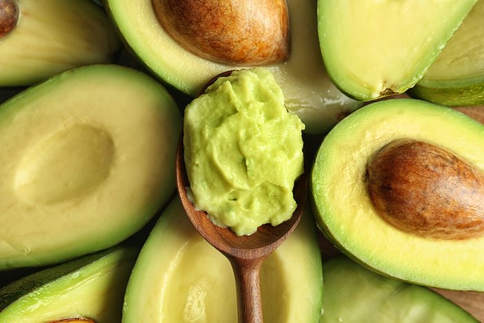 Spoon with guacamole on ripe avocados, top view