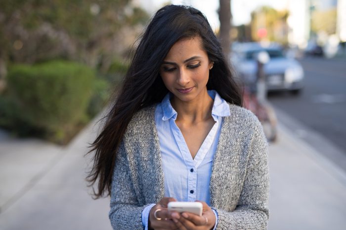 Indian woman in city walking texting cell phone