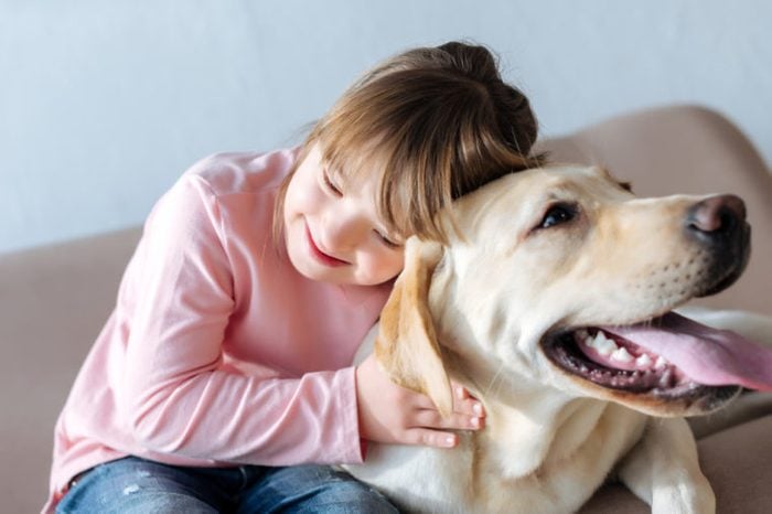 Happy child with down syndrome and Labrador retriever dog cuddling on sofa