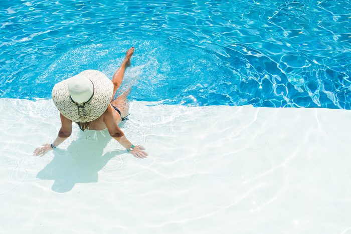 woman in hat sitting at the edge of a swimming pool