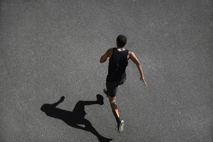 Top view of running man sprinting for success on run. Muscular runner or jogger dressed in black outfit, training at fast speed on black asphalt. Fit sport model exercising sprint outdoors