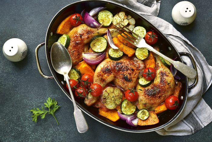 Chicken legs roasted with vegetables in a skillet pan over dark slate,stone or concrete background.Top view.