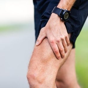 Runner leg and muscle pain during running training outdoors in summer nature. Health and fitness concept. Injured male jogger massage sore leg.