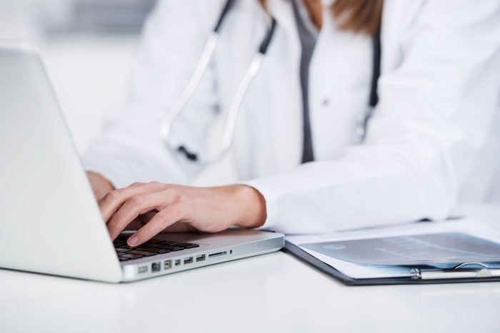Midsection of female doctor using laptop at desk