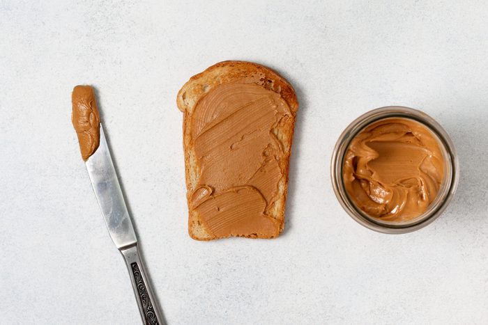 toast with peanut butter, jar of peanut butter, knife on a light gray background. view from above