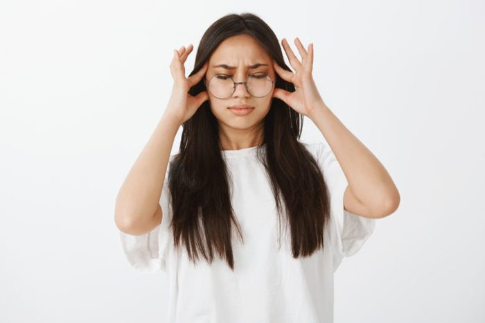Trying pull emotions together. Studio shot of displeased unhappy european woman in glasses, closing eyes and holding fingers on temple while suffering migraine or headache, waiting for painkillers