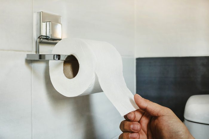 Hand picks a white toilet paper that hangs on the wall in the bathroom