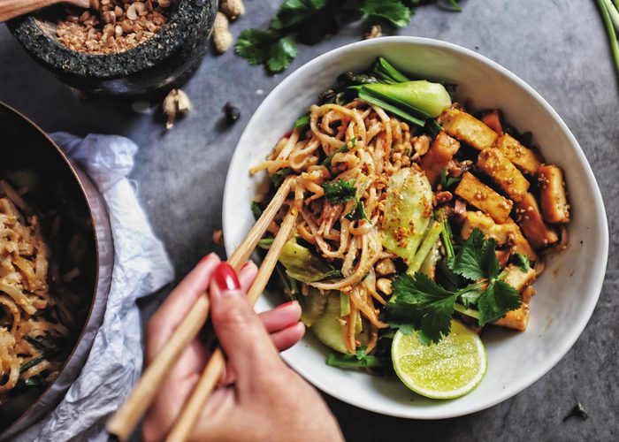  Udon with Padthai sauce, Healthy Vegetarian/vegan menu; Padthai noodle with smoke tofu and mixed vegetable - chinese baby Bok Choy , garlic chive, shallot and crushed peanut topping. chopstick hold.