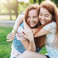 Young girl hugging her older sister smiling. Two red haired ladies having the best time of their lives.