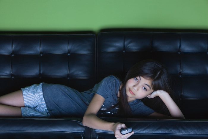 young girl lying on couch watching television