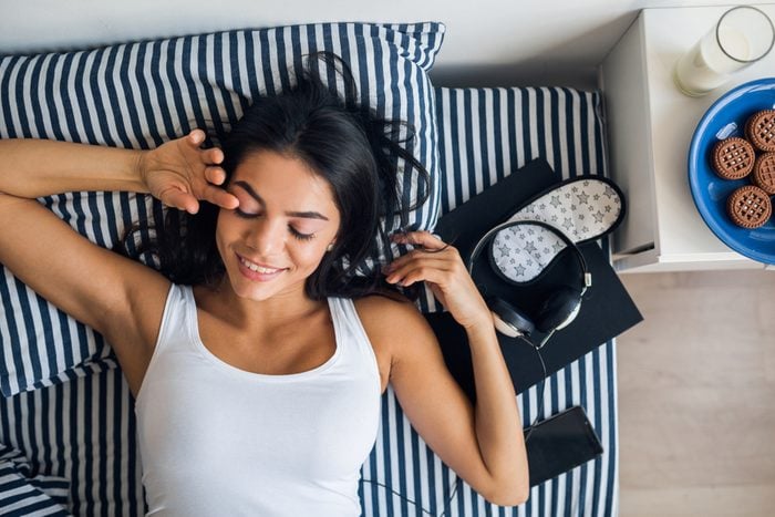 portrait of young attractive woman lying in bed smiling, view from above, wake up in morning, lazy, leisure time, sunday, relaxing, breakfast, phone, headphones, book, sleeping mask