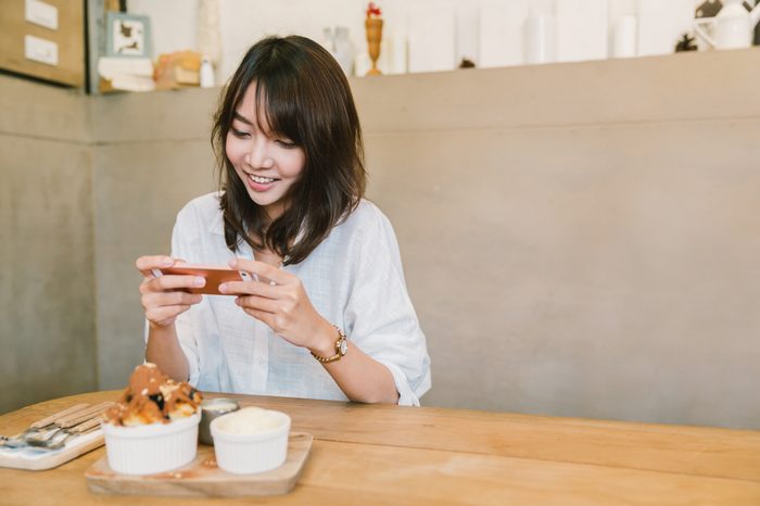 Beautiful Asian girl taking photo of chocolate toast cake, ice-cream, and milk at coffee shop. 