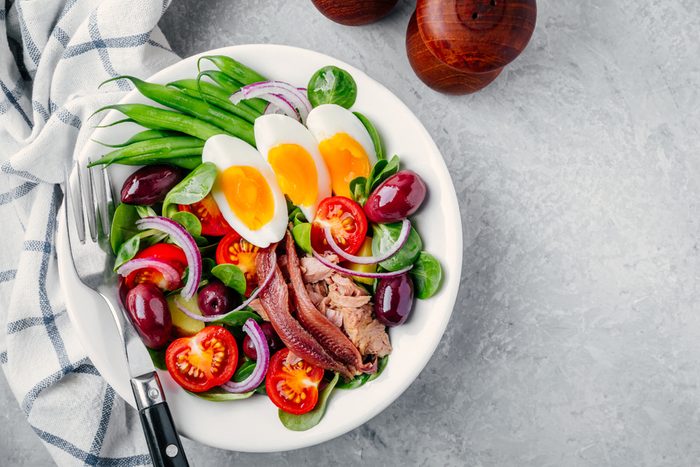 nicoise salad with tuna, anchovies, eggs, green beans, olives, tomatoes, red onions and salad leaves on gray background