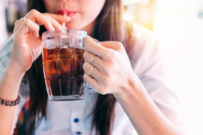Woman sipping iced cola with a straw from a glass mug.