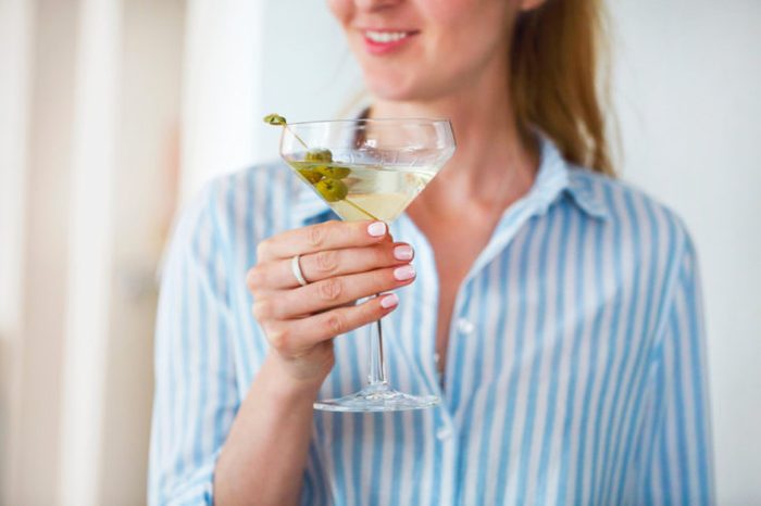 Woman holding glass with martini and green olives.