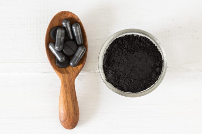 Activated charcoal powder in a glass bowl and pills on a spoon on white table