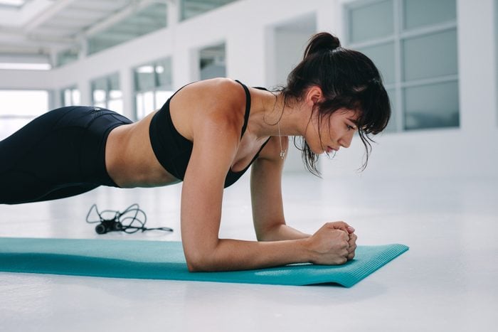 Muscular young woman doing plank exercise training at gym. Female exercising in fitness studio.