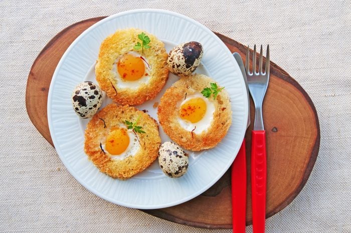 Small white plate topped with poached egg in a basket and quail eggs.
