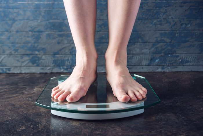 Female feet standing on electronic scales for weight control on dark background. The concept of sports training, diets and weight loss