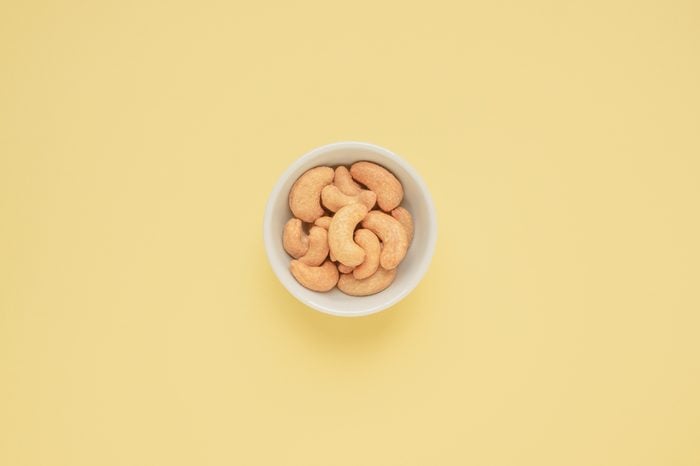 Cashew nuts in white cup on a beige background.