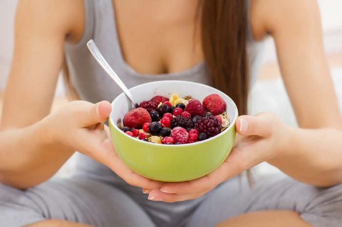 Young woman holding a bowl of granola topped with berries..