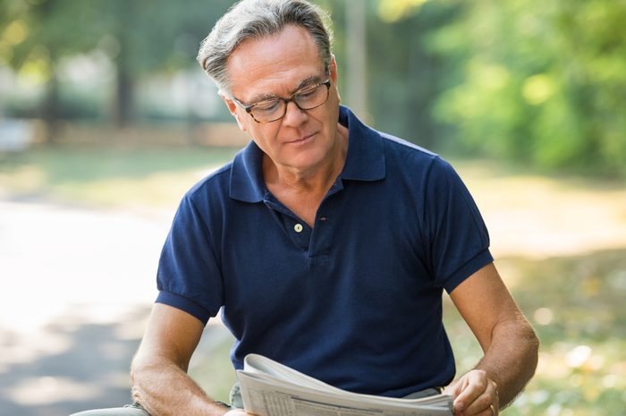 Senior man sitting at park and reading newspaper for aging brain