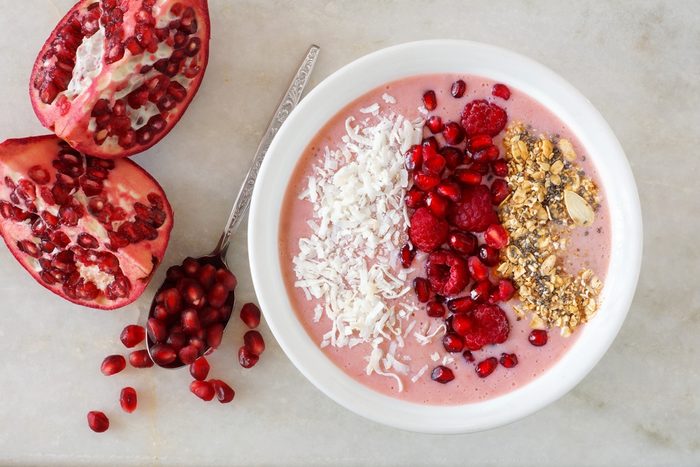 Smoothie bowl with pomegranates, raspberries, coconut and granola, overhead scene on marble