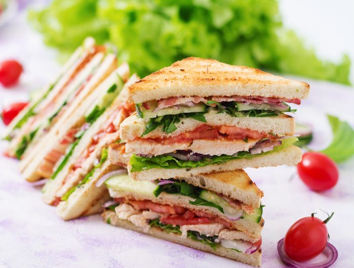 Club sandwich with chicken breast, bacon, tomato, cucumber and herbs.