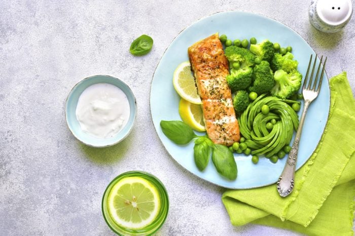 Grilled salmon garnished with green vegetables on a blue plate. 