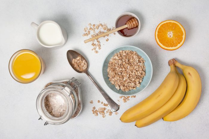 Oatmeal, milk, honey, orange, orange juice, bananas on a white countertop