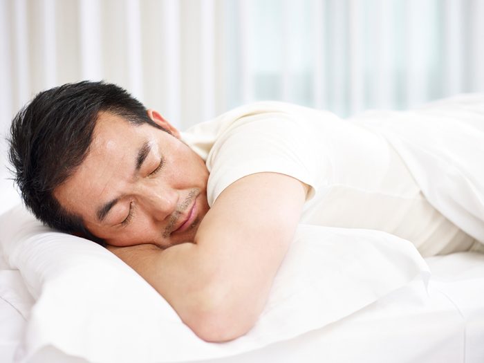 man lying on front in bed sleeping.