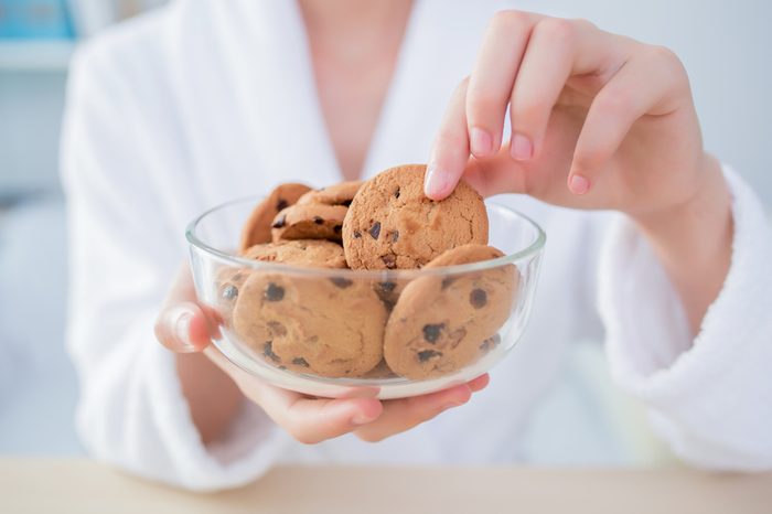 Woman at home grabs a chocolate chip cookie from a bowl.