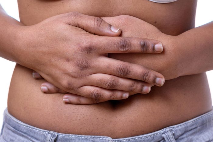 Mid section of dark-skinned woman holding her bare belly against white background