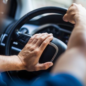 Close up shot of a man's hands holding a car's steering wheel and honking the horn.