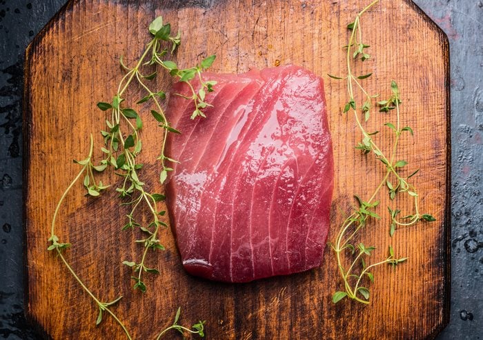 Tuna steak on rustic wooden background with fresh herbs, top view, close up. Seafood concept