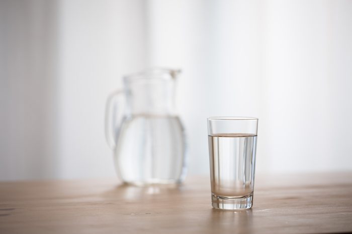 Glass of water and a pitcher of water in the background