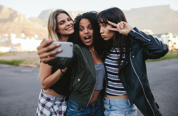 Happy female friends making selfie with smart phone. Multi ethnic group of women hanging out in the city and taking self portrait with mobile phone.