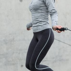 fitness, sport, people, exercising and lifestyle concept - close up of woman skipping with jump rope outdoors