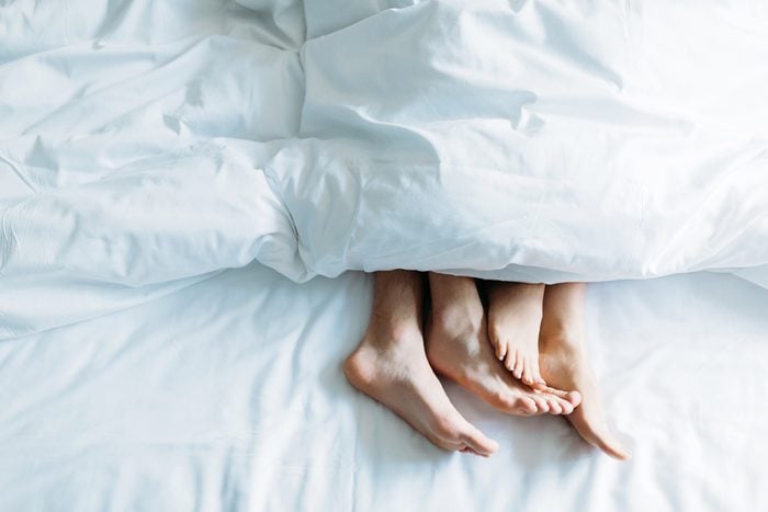couple's feet under a comforter in bed